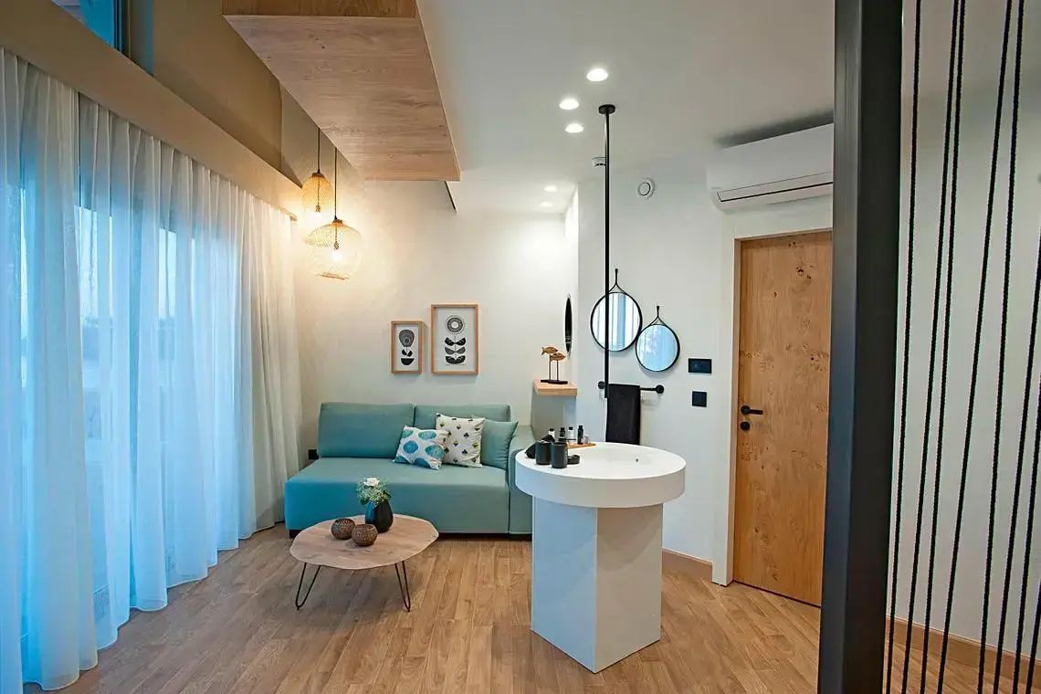 Modernes Hotelzimmer mit blauem Sofa, Holztisch und freistehendem Waschtisch im Raum.