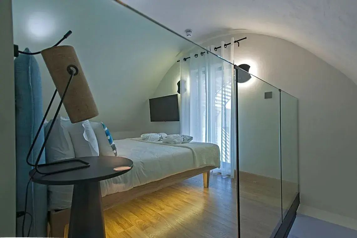 Schlafbereich auf einer Galerie mit Holzfußboden, Bett und Glasbrüstung.