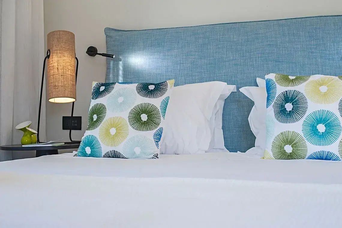 Nahaufnahme eines weiß gemusterten Kissens auf einem Bett mit blauem Kopfteil aus Stoff.