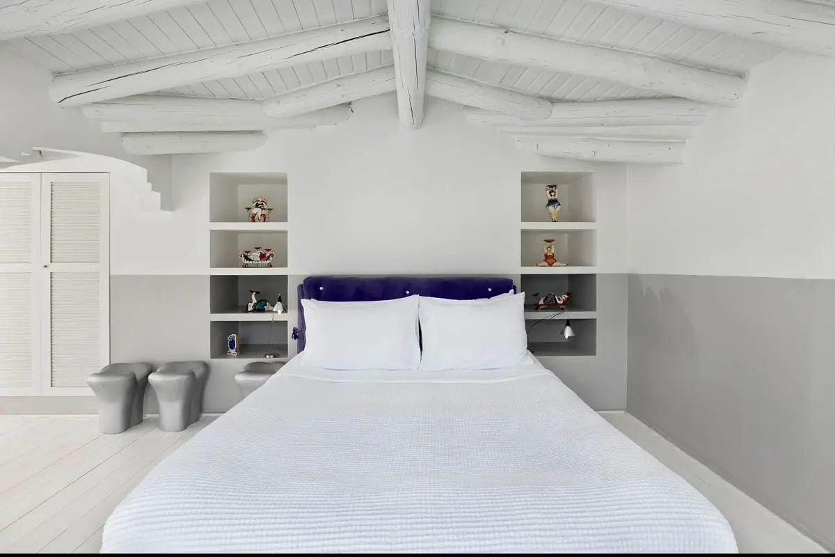 Doppelbett unter einer weißen Holzbalkendecke mit Nischen in der Wand.
