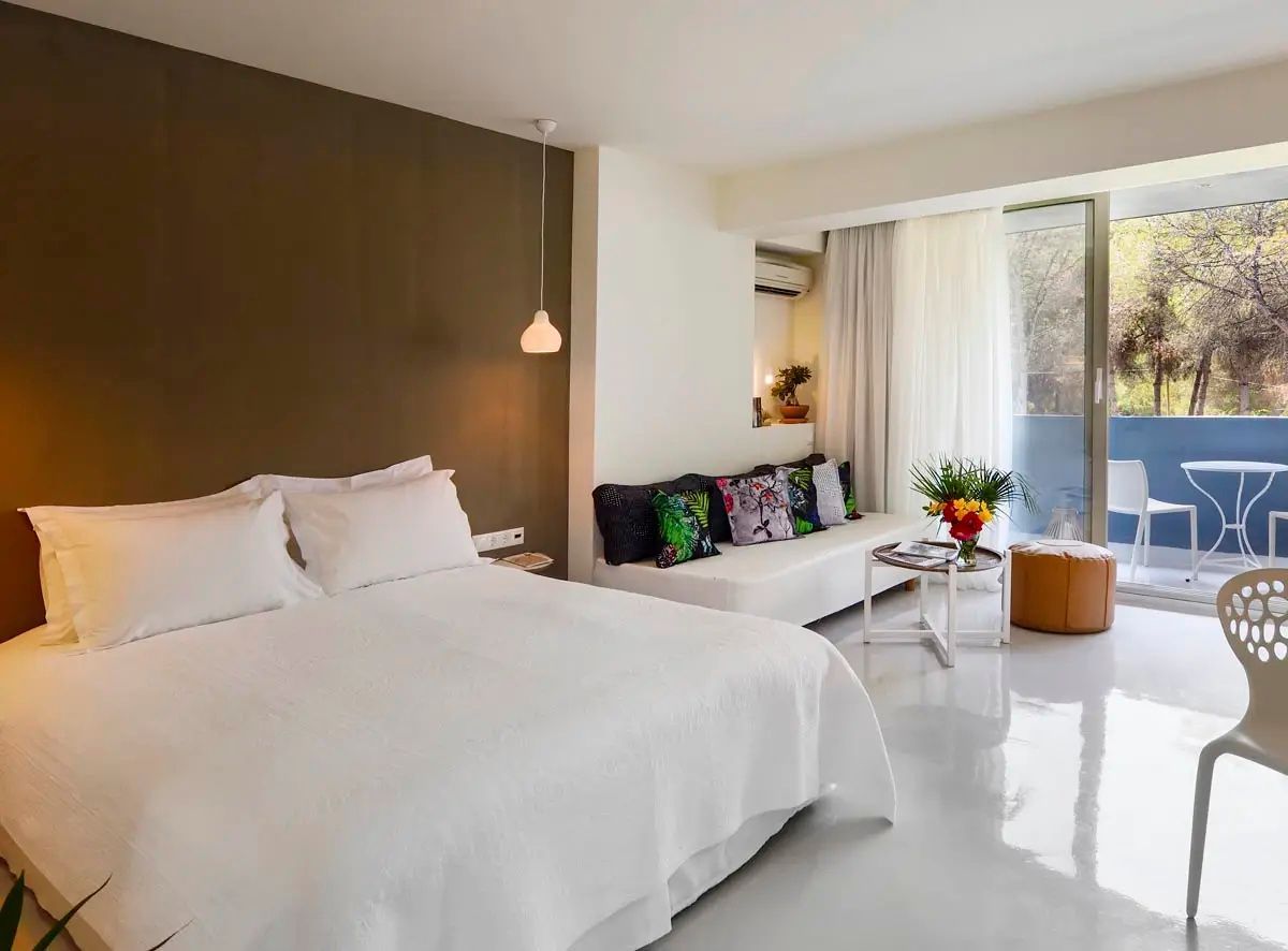 Hell eingerichtetes Zimmer mit weißem Doppelbett, Sofa und brauner Akzentwand.