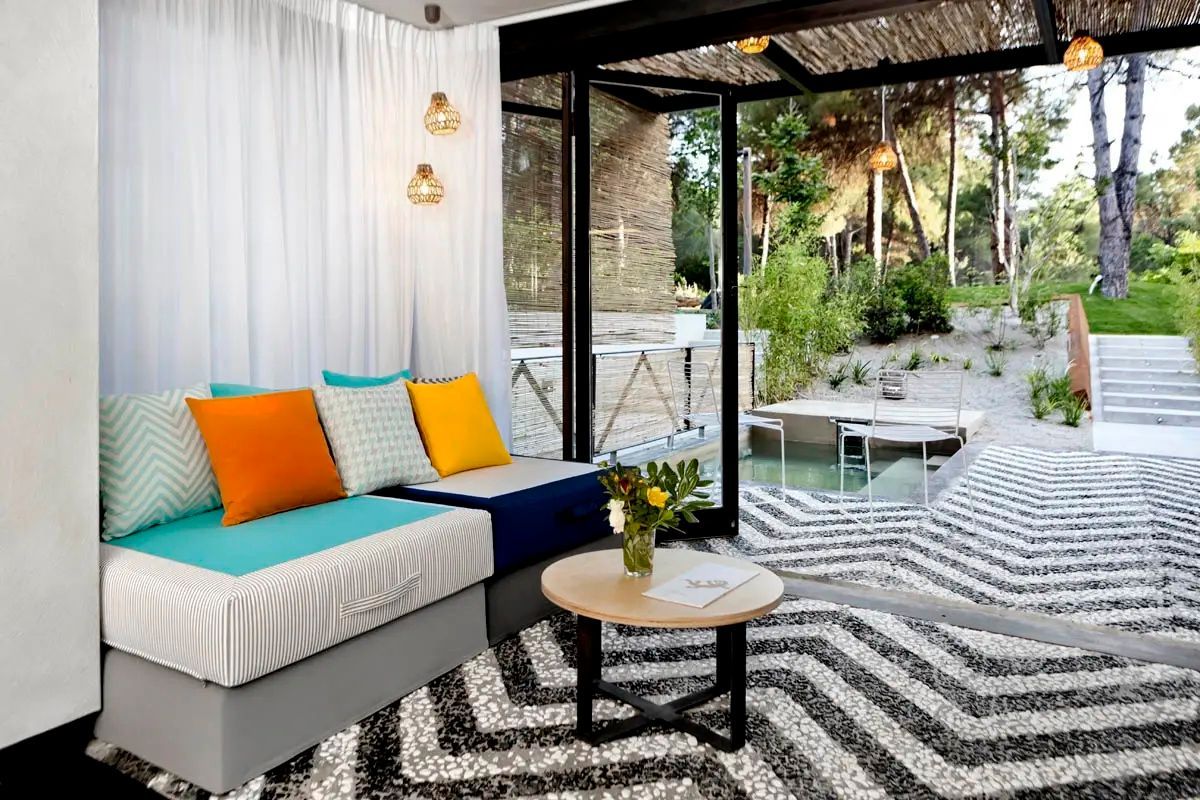 Sitzbereich mit bunten Kissen und Couchtisch neben einer geöffneten Glasfront zum Garten.