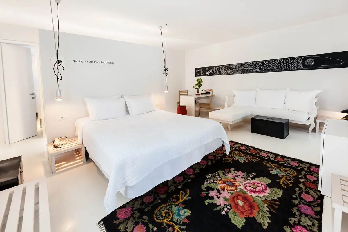 Weiß gestaltetes Hotelzimmer mit einem Bett, schwarzem Teppich und Wanddekoration.