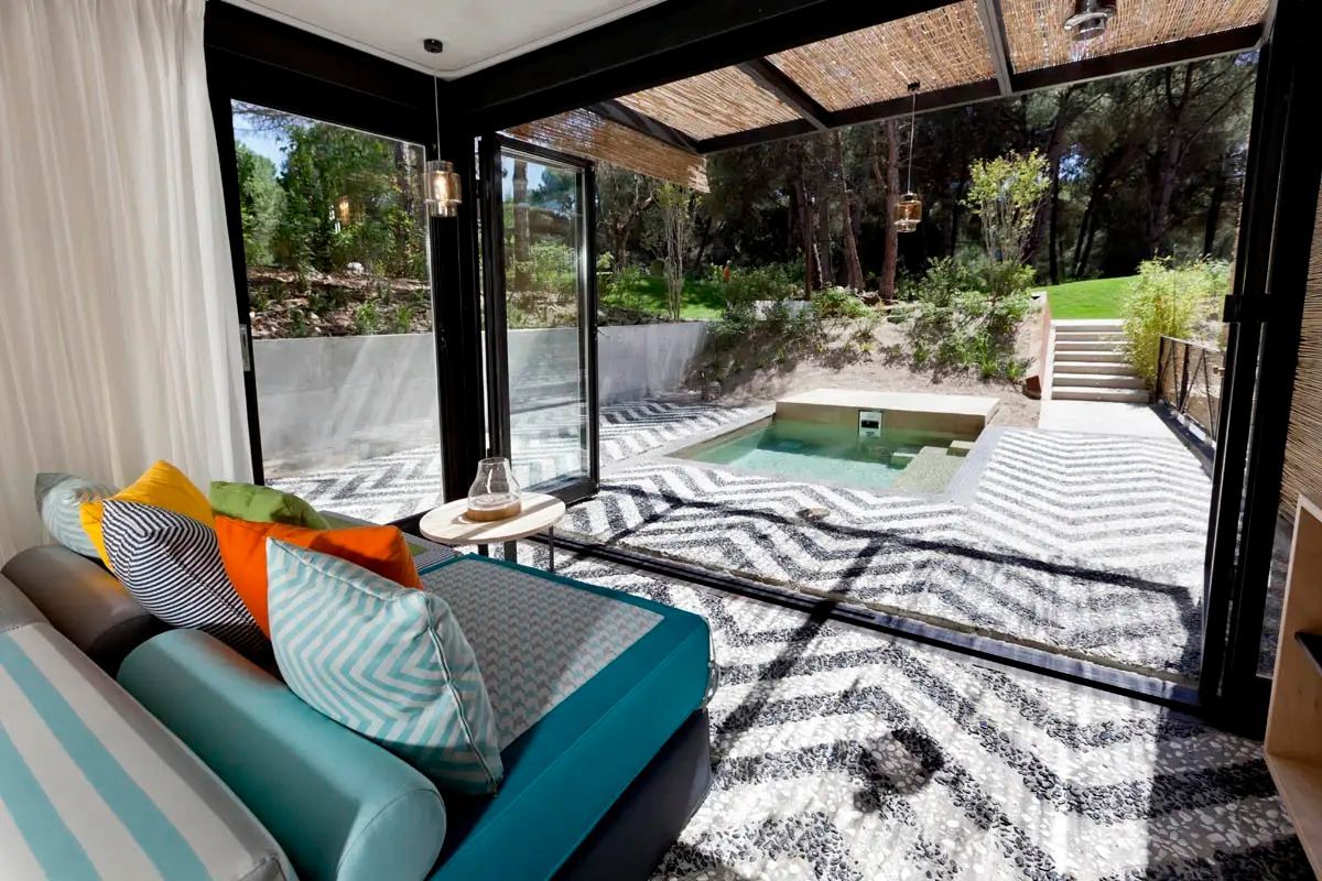 Blick durch eine geöffnete Glasfront auf eine Terrasse mit privatem Pool und Bäumen.
