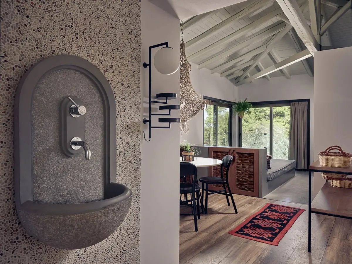 Blick in einen Wohnbereich mit Steinwaschbecken an der Wand und Esstisch.