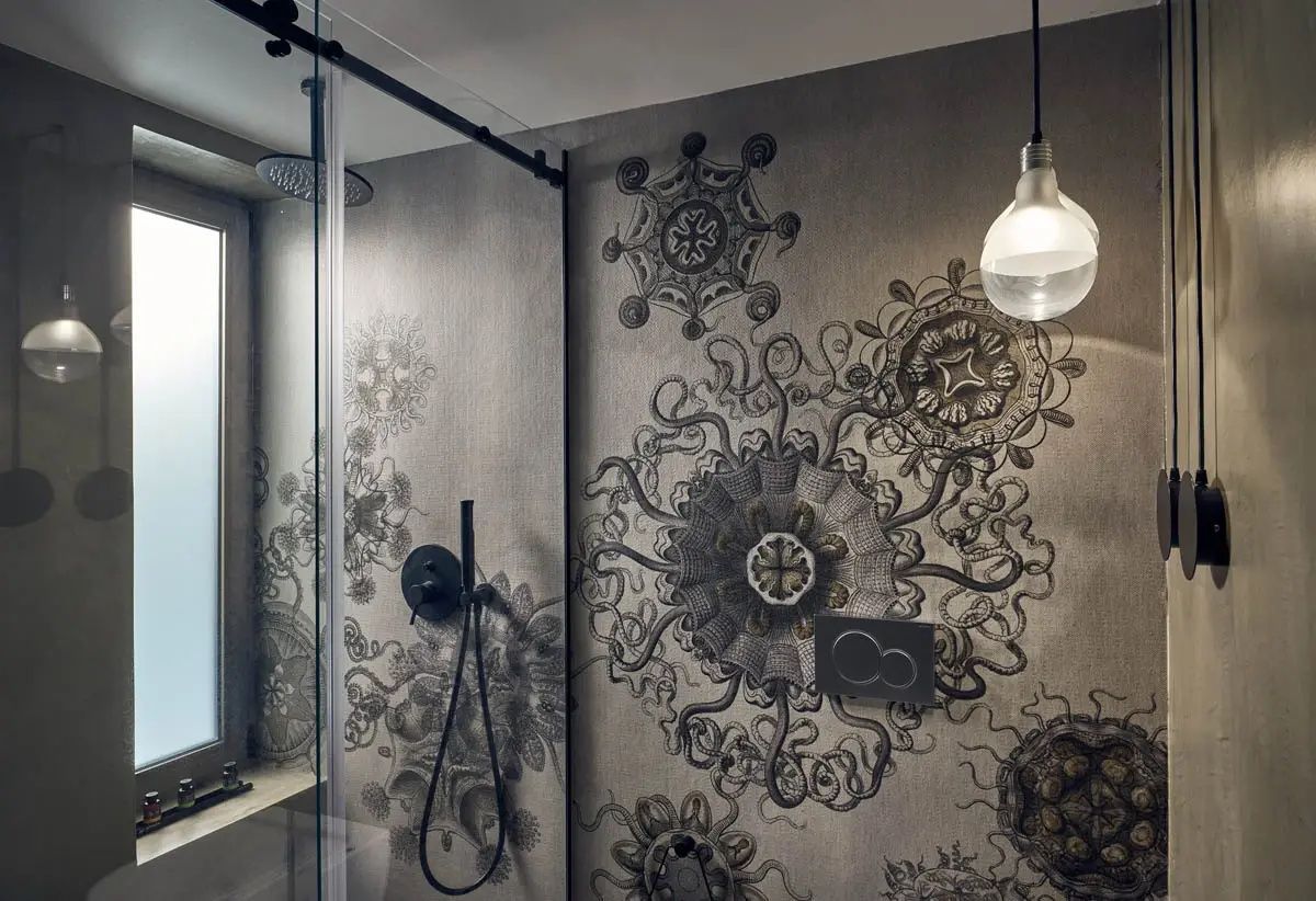 Badezimmer mit gemusterten Wandfliesen, Duschbereich und dunkler Armatur.