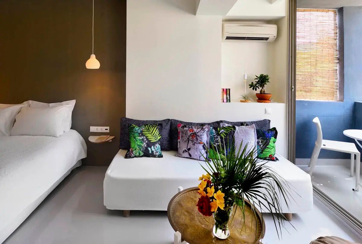 Sitzecke im Hotelzimmer mit weißem Sofa, bunten Kissen und einem Blumenstrauß.