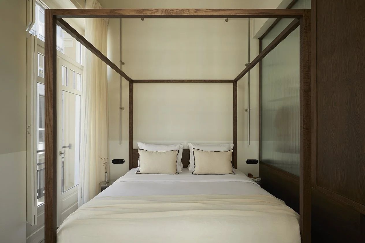 Himmelbett aus dunklem Holz mit hellen Kissen und weißer Bettwäsche im Hotelzimmer.