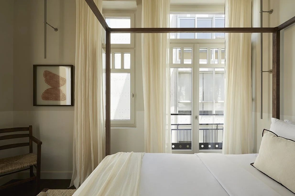 Blick vom Bett auf große Fenster mit hellen Vorhängen und französischem Balkon.