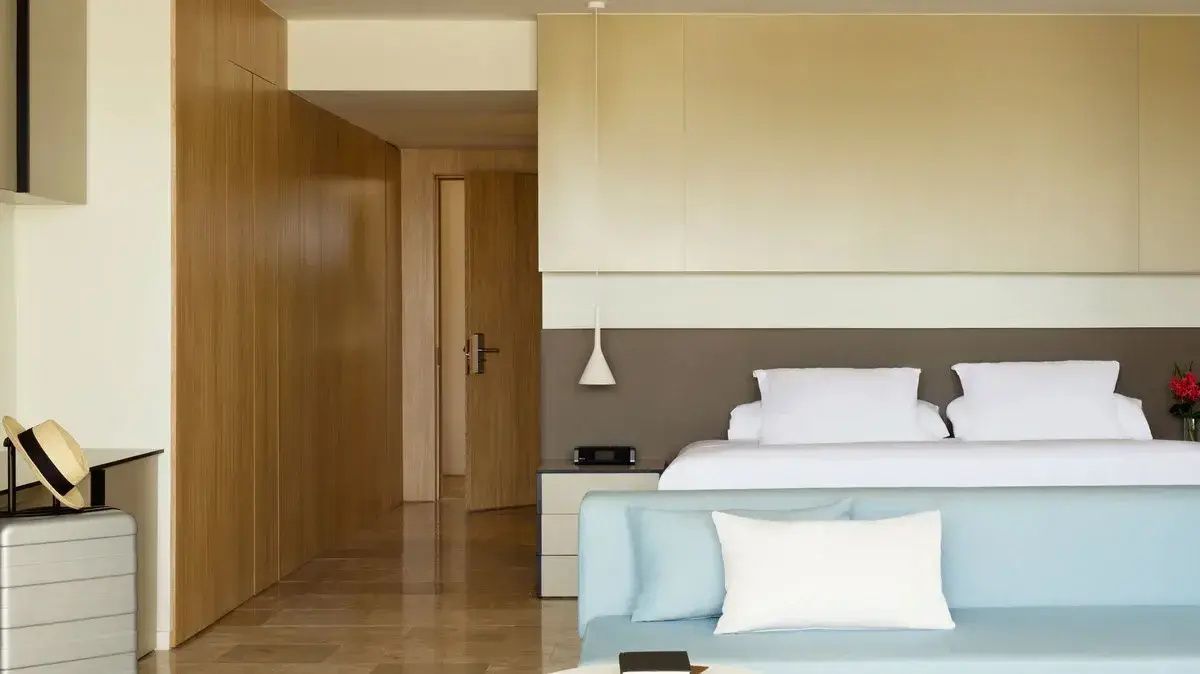 Helles Hotelzimmer mit weißem Doppelbett, blauem Sofa und einer Wandverkleidung aus Holz.