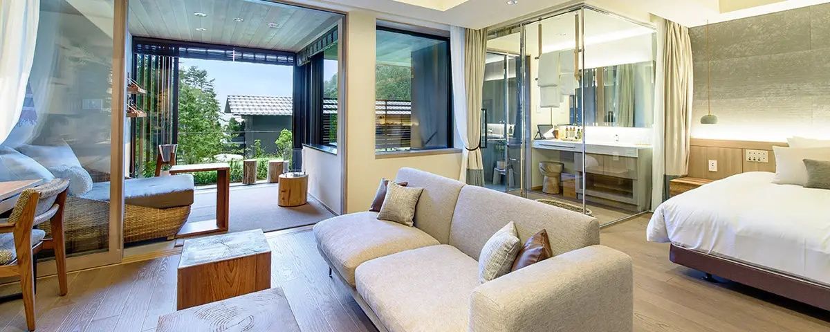 Moderner Wohnbereich mit hellem Sofa, Holzboden und Blick auf den angrenzenden Balkon sowie das Badezimmer.