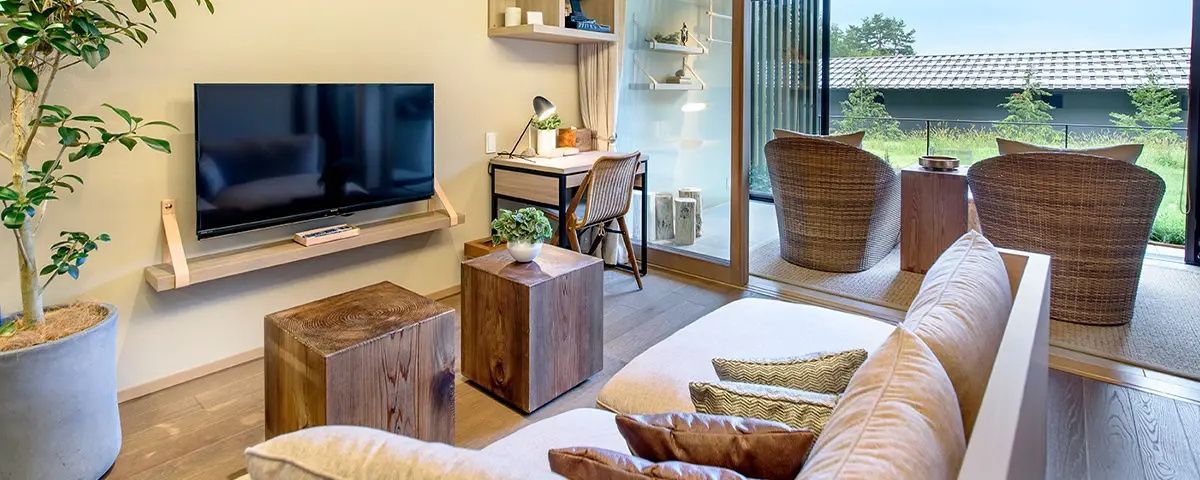 Kleiner Arbeitsplatz aus Holz neben einem Fernseher und Beistelltischen im Hotelzimmer.