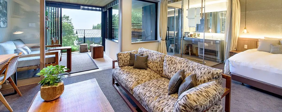 Gemustertes Sofa im Sitzbereich einer Suite mit großen Fensterfronten und Balkon.