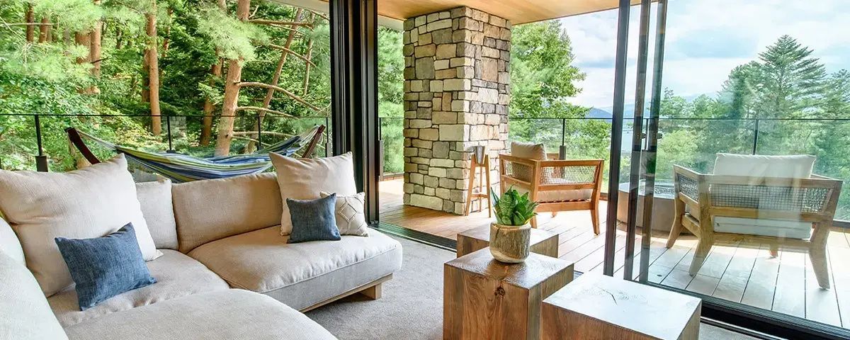 Wohnbereich mit hellem Sofa und Blick auf den überdachten Holzbalkon mit Natursteinpfeiler.