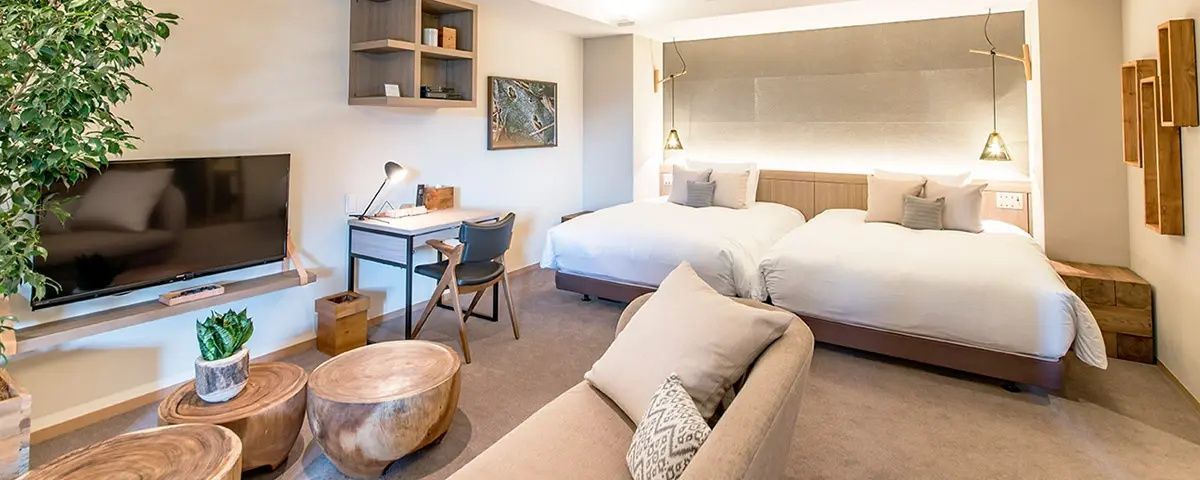 Hotelzimmer mit zwei zusammenstehenden Betten, einem Sofa im Vordergrund und Schreibtisch.