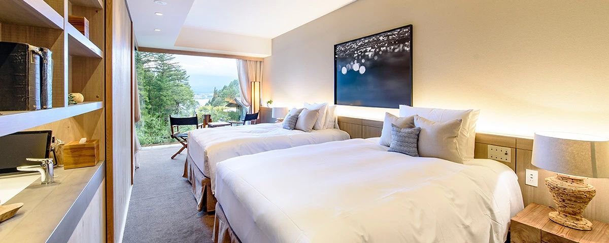 Zwei Betten im Hotelzimmer mit großem Kunstwerk an der Wand und Blick ins Grüne.