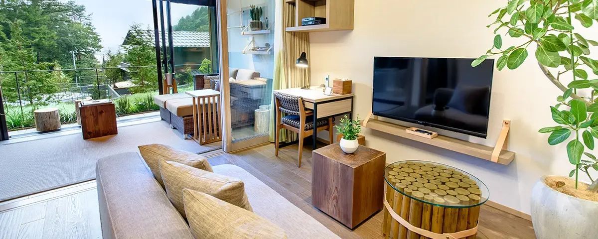 Wohn und Arbeitsbereich im Zimmer mit Holzmöbeln, Fernseher und Durchgang zur Terrasse.