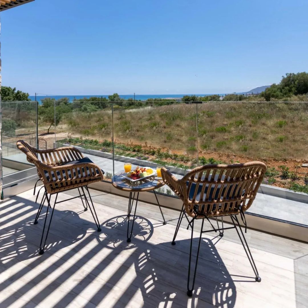 Sonniger Balkon mit Sitzgelegenheiten, kleiner Speise-Ablage und Blick auf die Landschaft und das Meer.