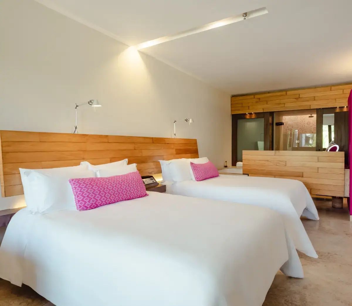 Hotelzimmer mit zwei Doppelbetten, rosa Kissen und einer Kopfteil-Verkleidung aus Holz.