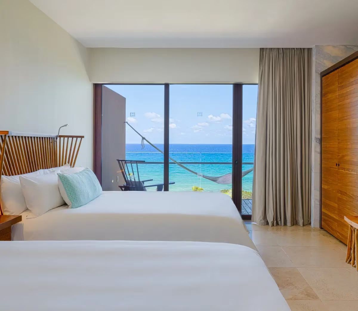 Hotelzimmer mit zwei Betten und Glasfront mit Meerblick sowie Hängematte auf dem Balkon.