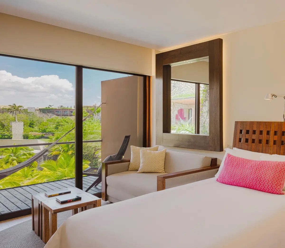 Helles Hotelzimmer mit Bett, Sofa und Balkonzugang mit Blick ins Grüne.