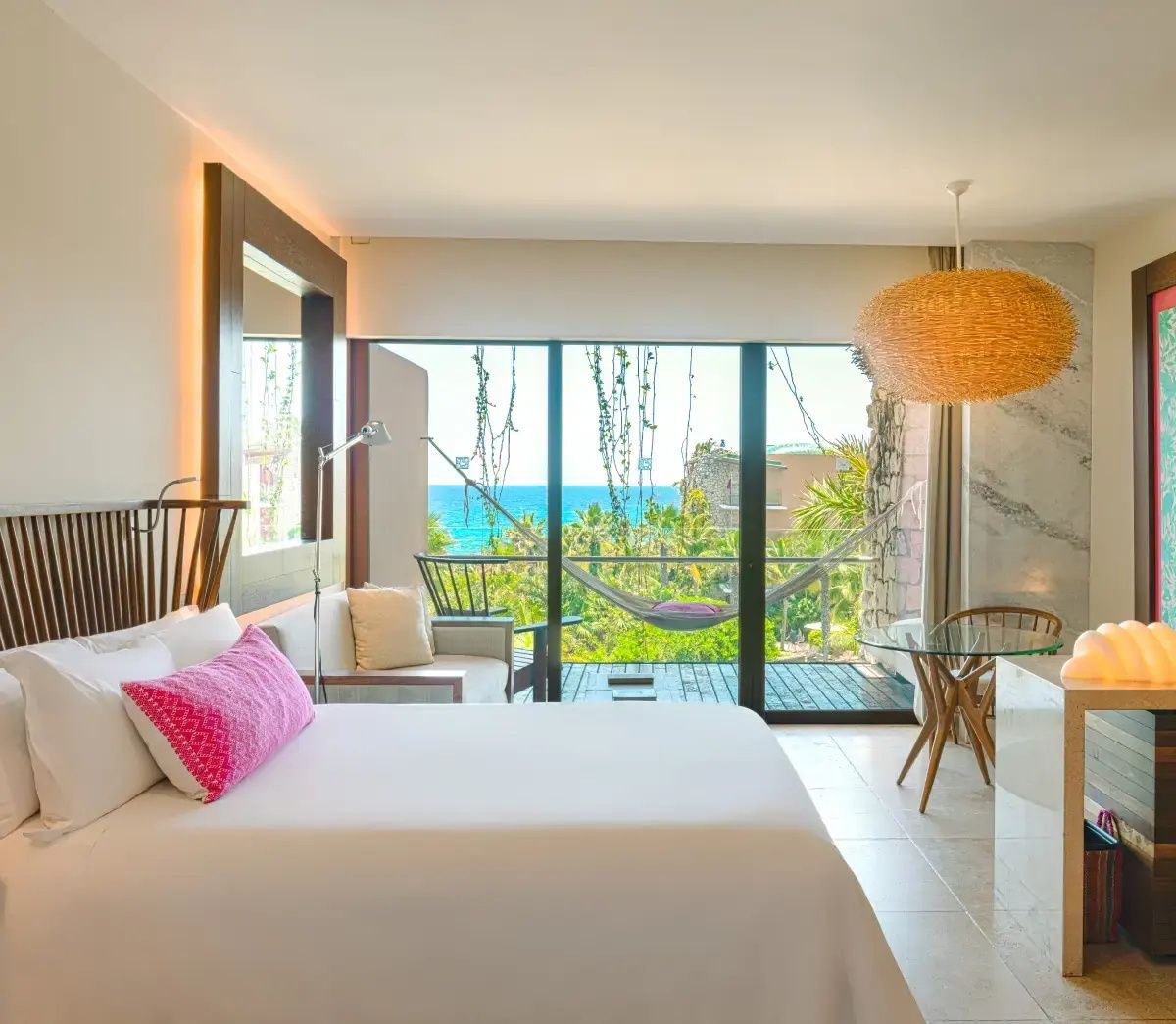 Blick aus dem Hotelzimmer über den Balkon mit Hängematte auf das Meer und Palmen.