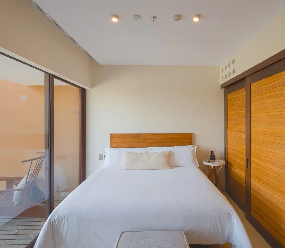 Doppelbett mit weißer Bettwäsche, Holz Kopfteil und Zugang zum Balkon im Zimmer.