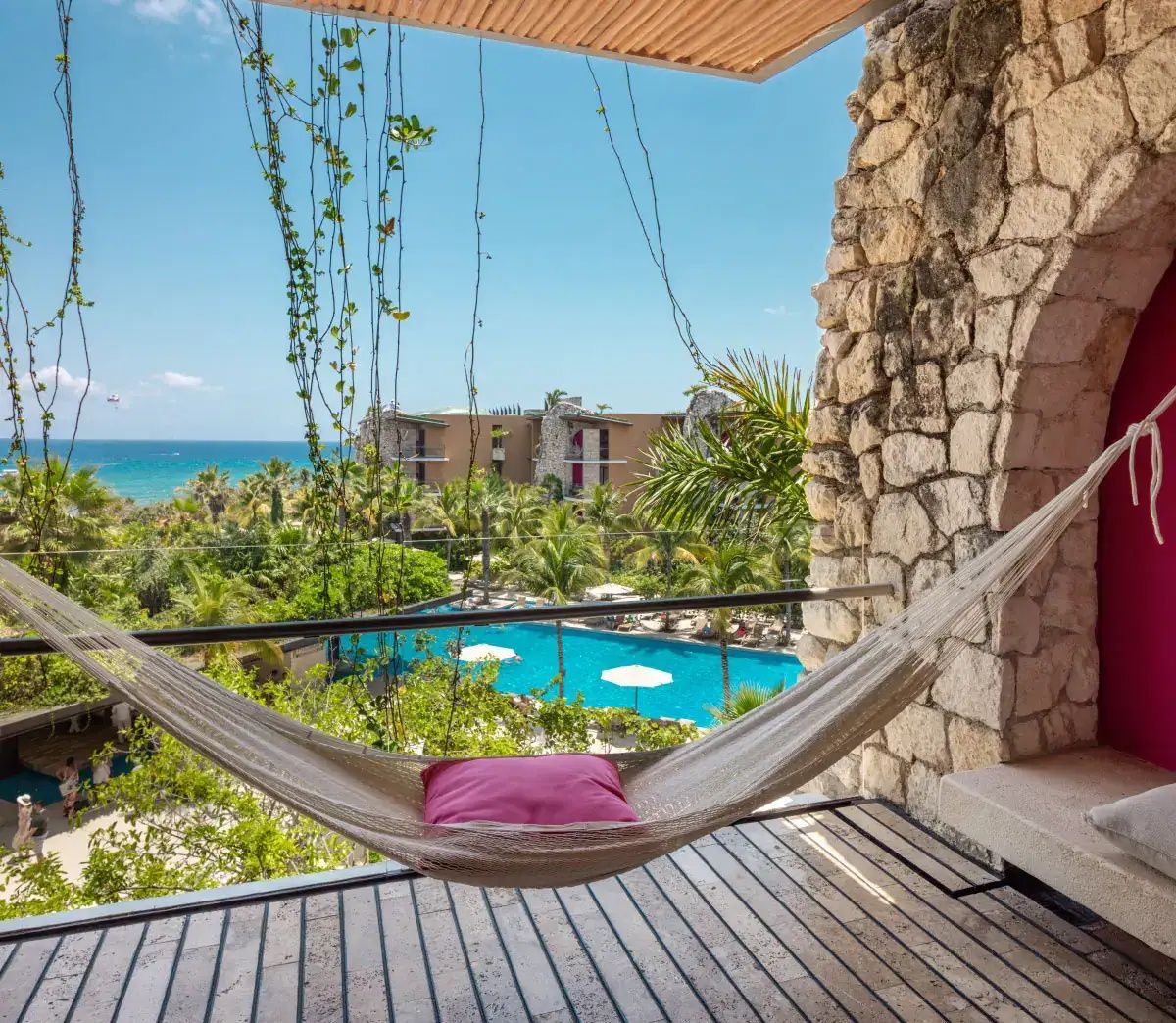 Terrasse mit Hängematte und Ausblick auf einen Außenpool, Palmen und das Meer.