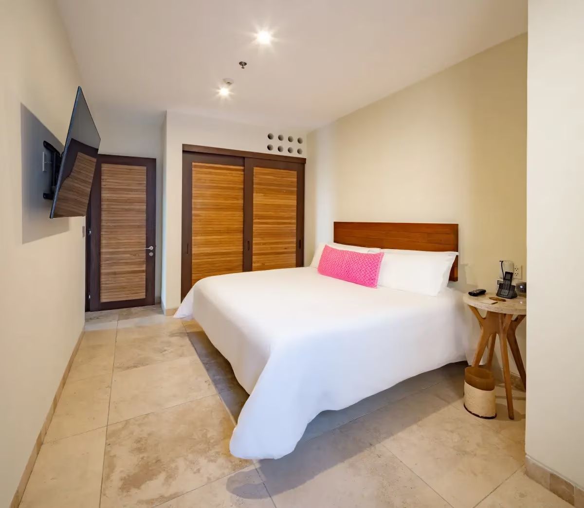 Helles Schlafzimmer mit großem Doppelbett, pinkem Akzentkissen und Holzschrank.