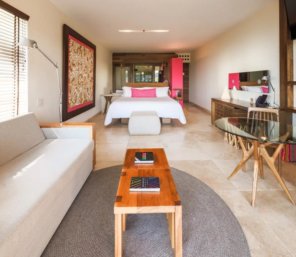 Geräumiges Hotelzimmer mit weißem Doppelbett, gemütlichem Sofa und einem runden Teppich.