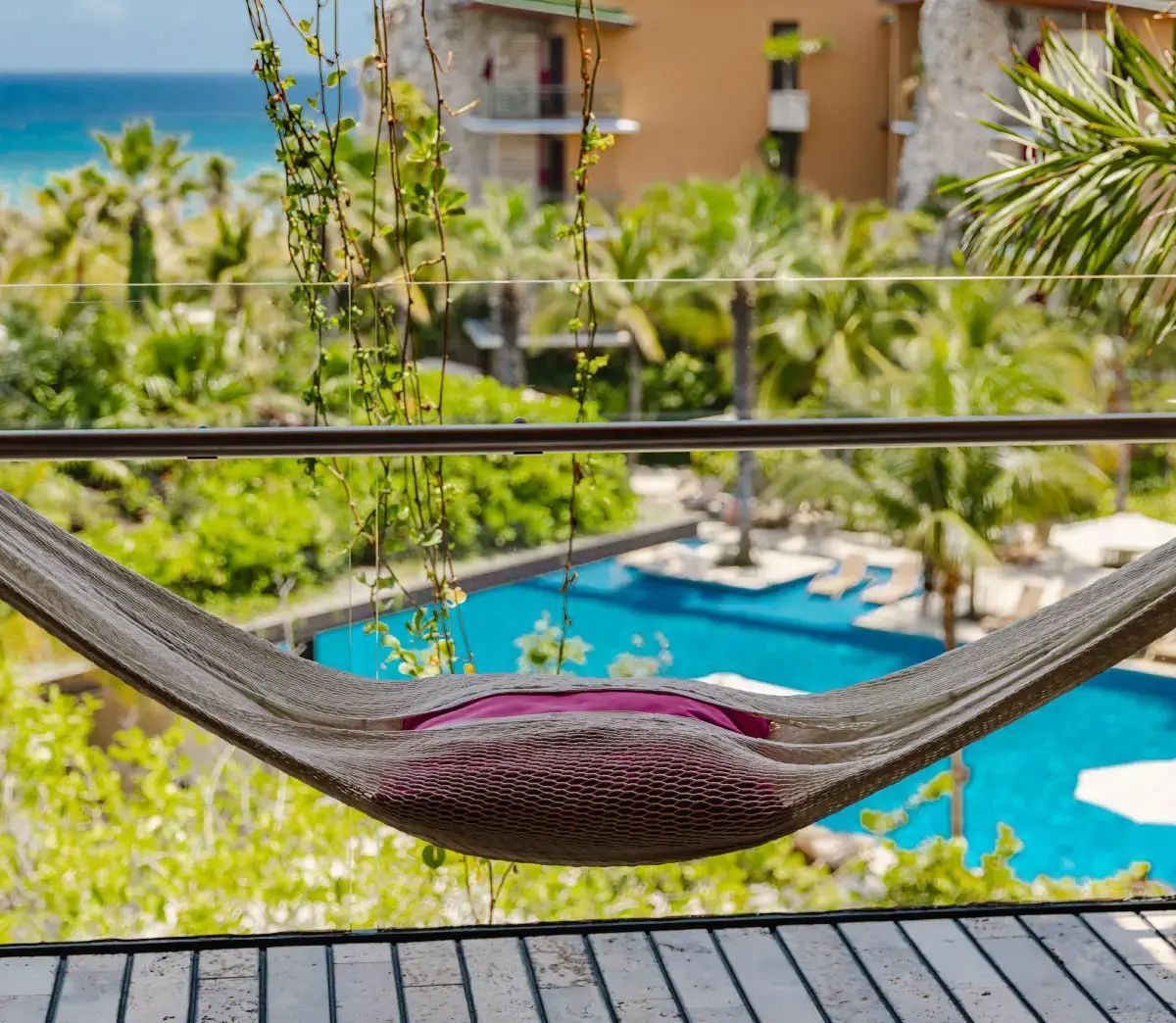 Blick von einer Hängematte auf dem Balkon auf einen Pool im Tropengarten und das Meer.
