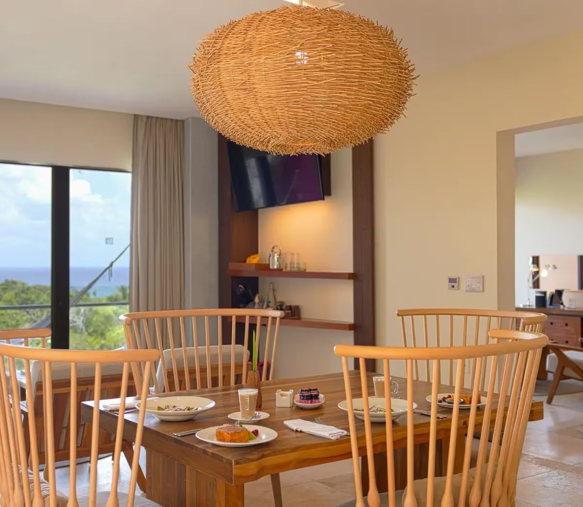 Esstisch aus Holz mit Stühlen und einer gewebten Lampe im Wohnbereich der Suite.