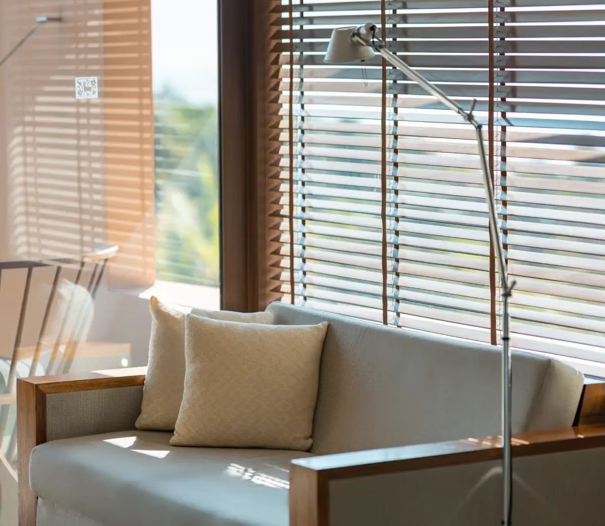 Sofa mit zwei Kissen neben einer Stehlampe vor einem Fenster mit Holzjalousien.