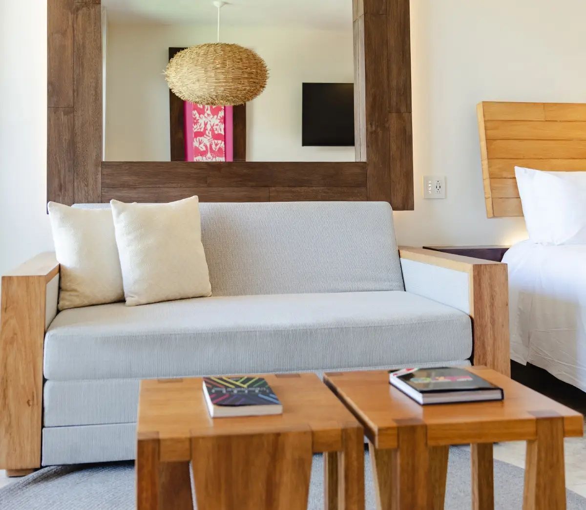Sitzbereich im Hotelzimmer mit hellem Sofa, Holz-Couchtischen und großem Spiegel.