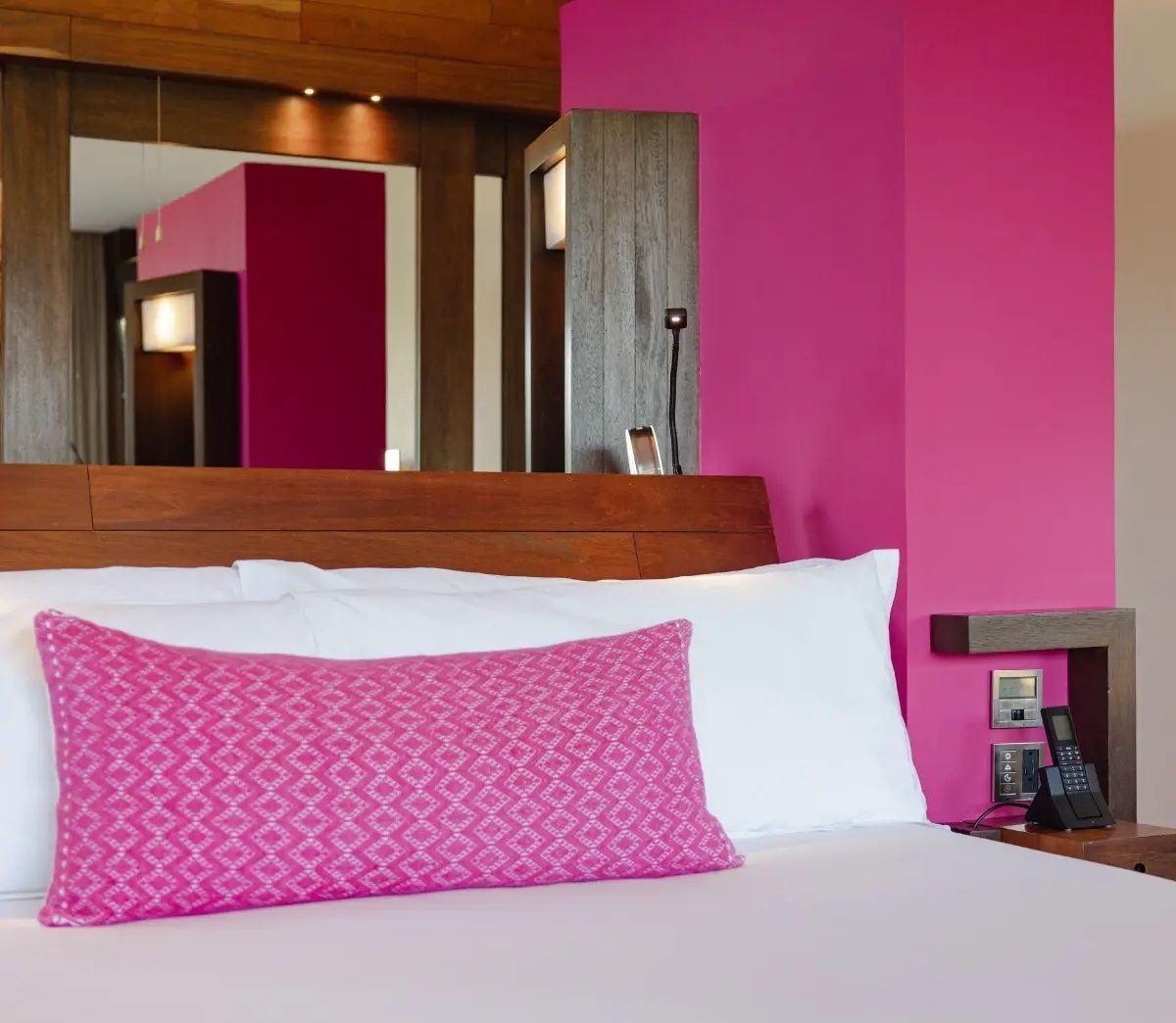 Bett im Hotelzimmer mit weißer Wäsche, rosa Kissen und farbiger Wandgestaltung.