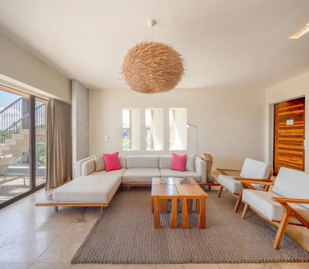 Sitzbereich mit hellem Sofa, rosa Kissen, Holztischen und Teppich im Zimmer.