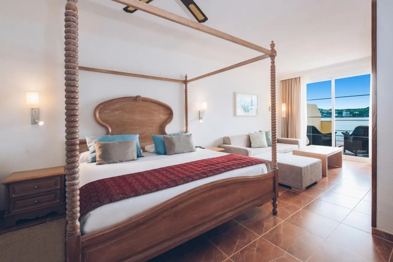 Himmelbett aus Holz mit Kissen und angrenzendes Sofa im hell eingerichteten Hotelzimmer.
