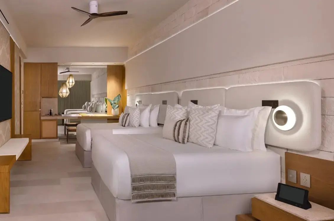 Helles Hotelzimmer mit zwei Doppelbetten, weißer Bettwäsche und Deckenventilator.