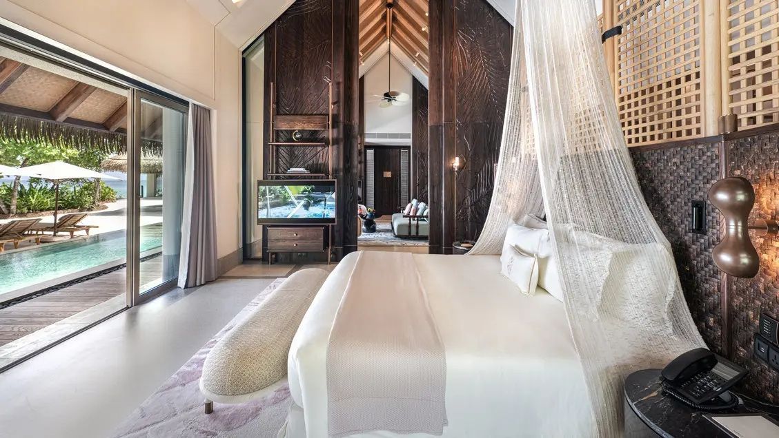 Schlafbereich einer Villa mit Doppelbett, Moskitonetz und Holzverkleidung an den Wänden.