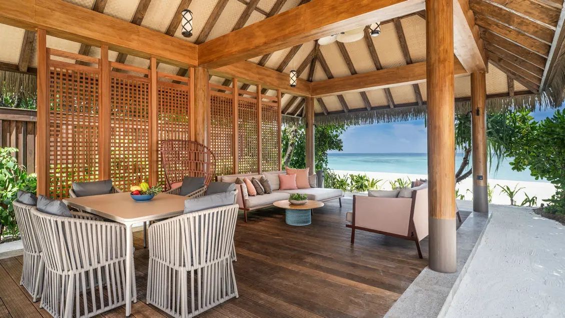 Überdachte Terrasse mit Sitzecke und Esstisch mit Blick auf den Strand und das Meer.