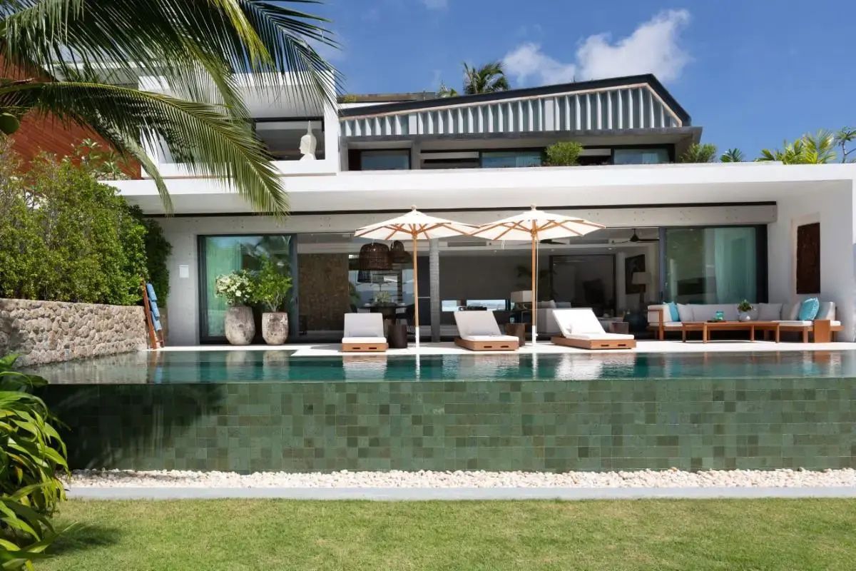 Außenansicht der zweistöckigen Villa mit einem Infinitypool, Sonnenliegen und Schirmen.