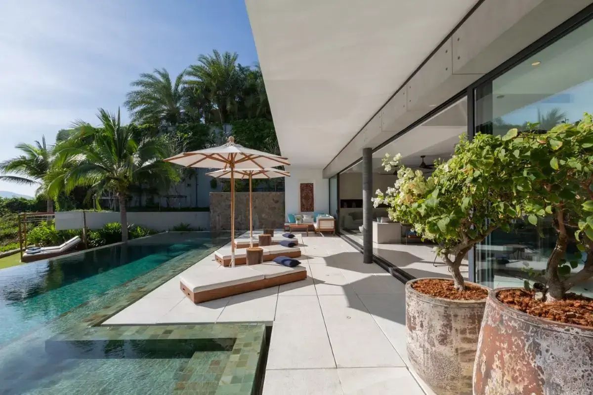 Sonnendeck mit Liegestühlen und Schirmen am Pool vor der geöffneten Villa