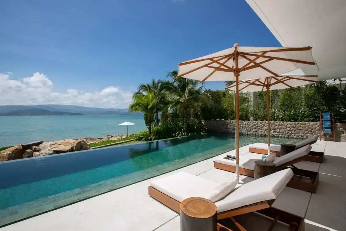 Infinitypool auf einer Terrasse mit zwei Sonnenliegen, Sonnenschirmen und Blick auf das Meer.