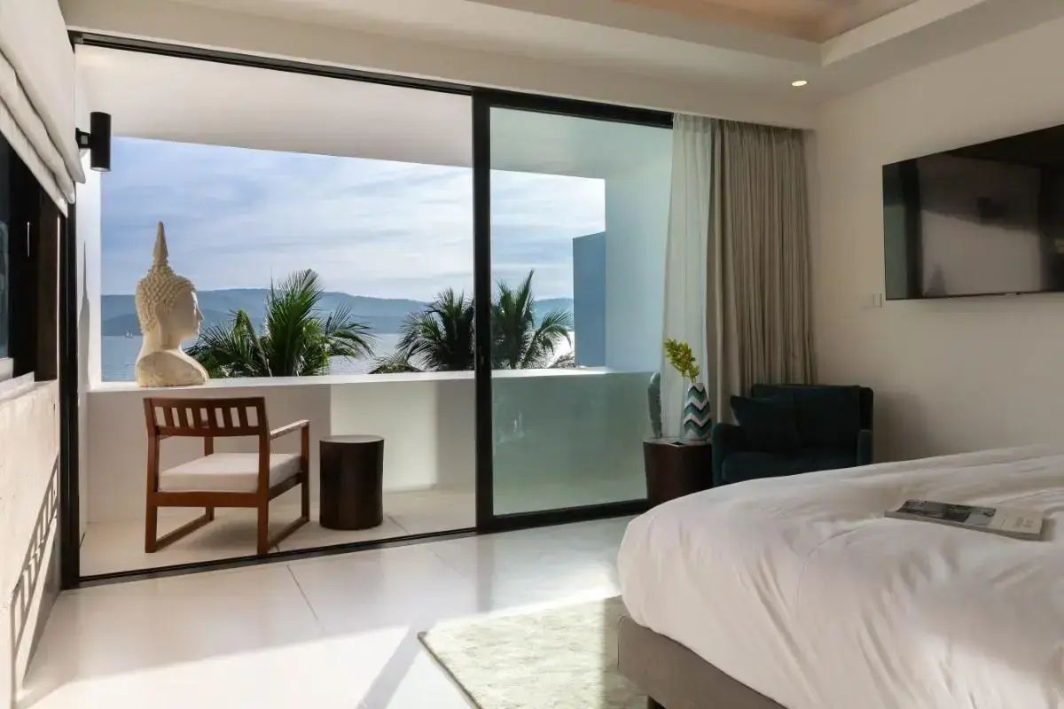 Blick vom Schlafzimmer über eine Terrasse auf das Meer und gegenüberliegende Hügel.