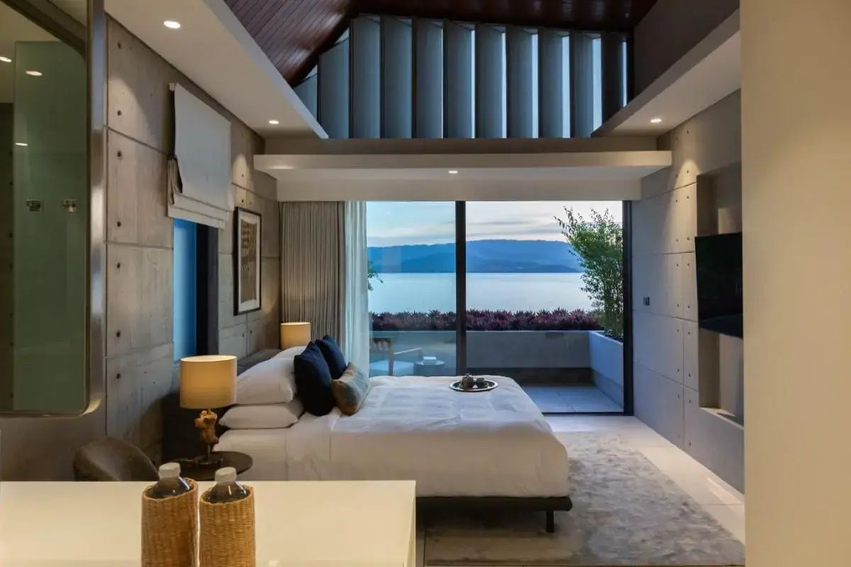 Blick aus dem Schlafzimmer durch große Glasfenster auf das Meer und Inseln.