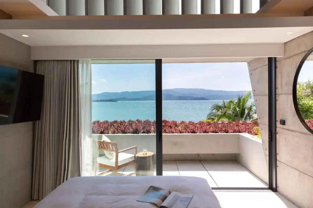Aussicht aus dem Zimmer auf den Balkon mit Meerblick und rot blühenden Pflanzen.