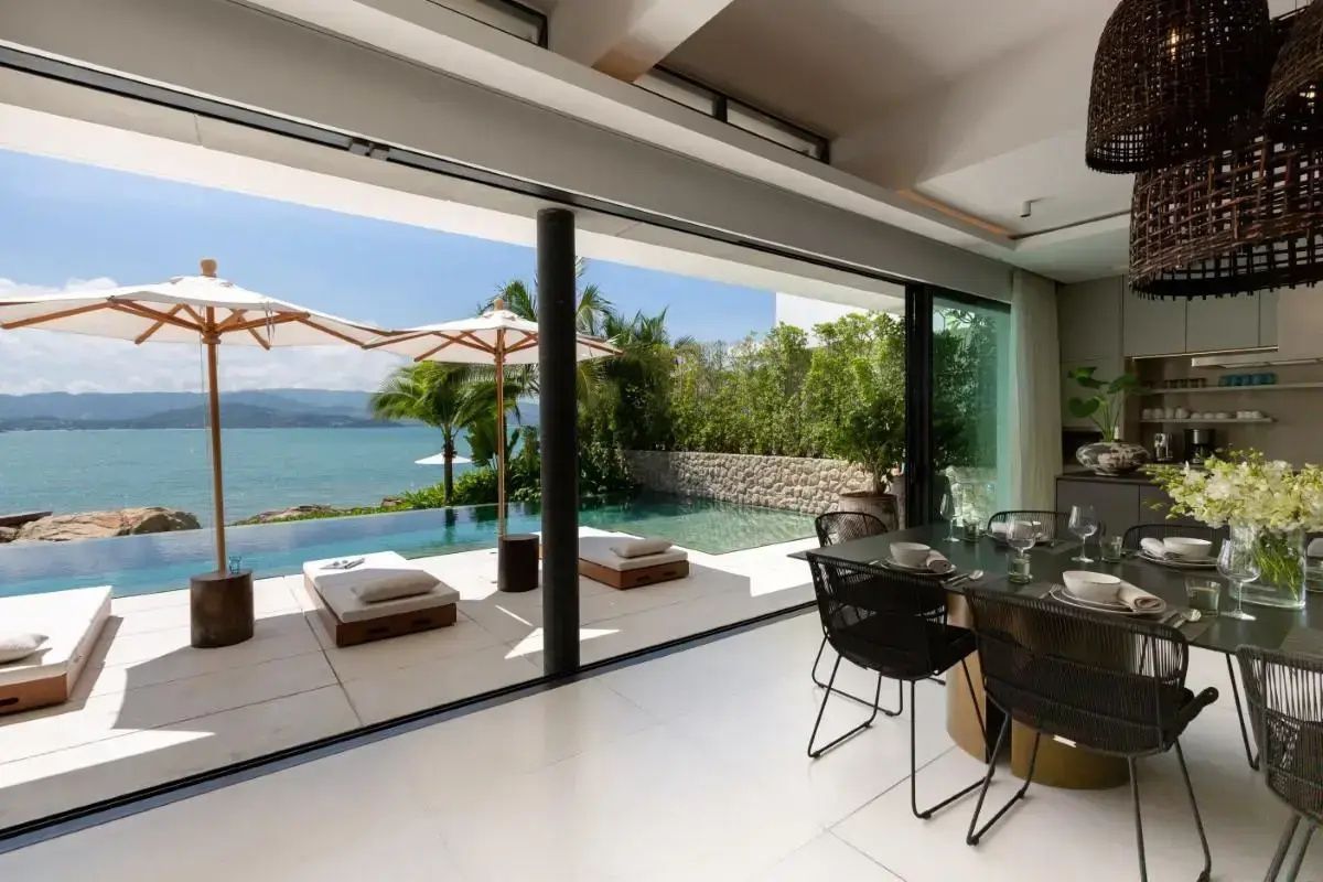 Blick durch geöffnete Glasfront auf Terrasse mit Pool, Sonnenliegen und das Meer.