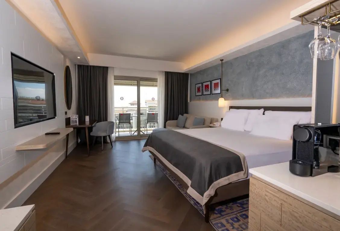 Modern eingerichtetes Hotelzimmer mit großem Doppelbett, Sofa und Balkonzugang.