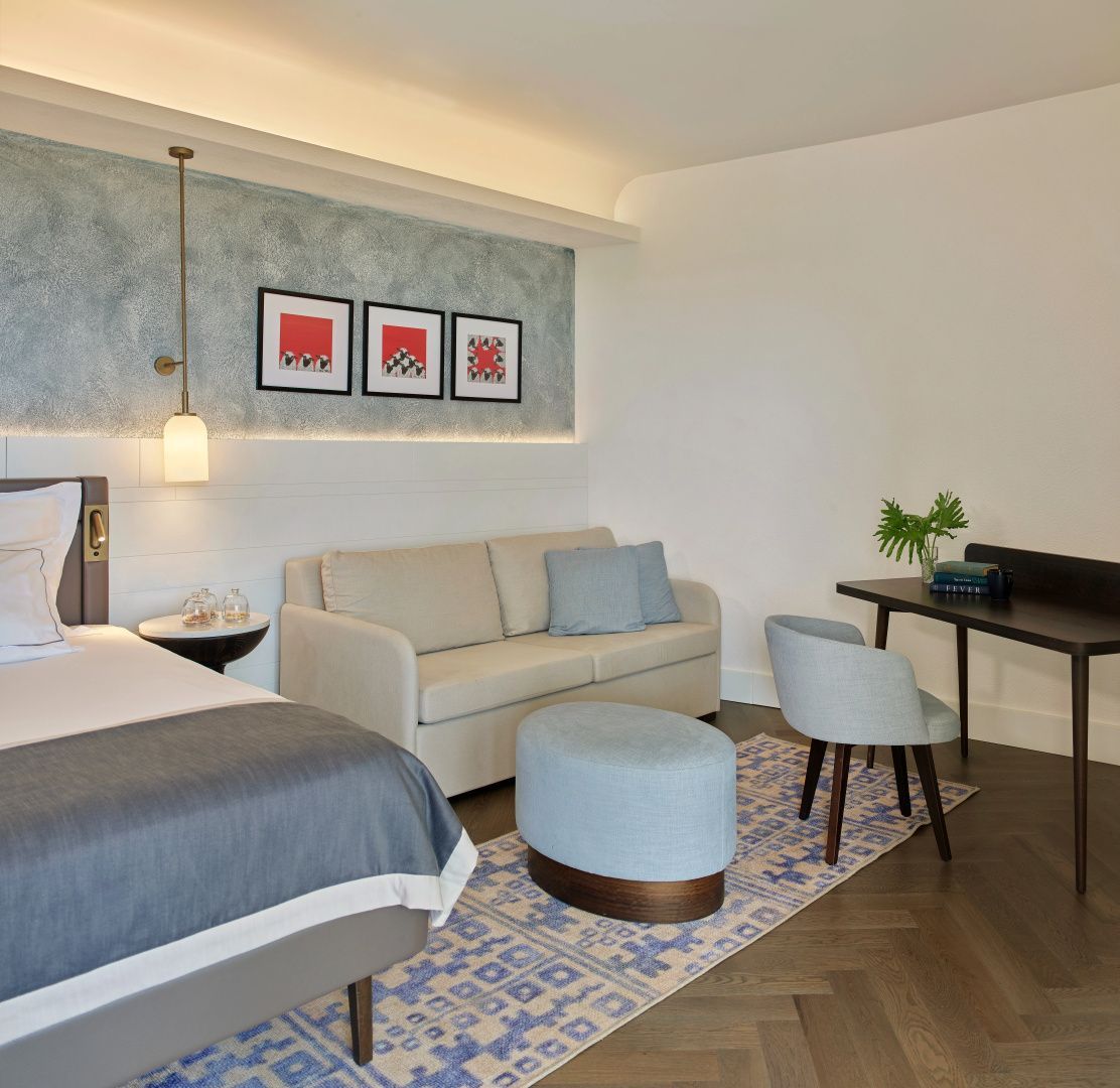 Wohnbereich eines Hotelzimmers mit Sofa, Hocker und einem kleinen Schreibtisch.