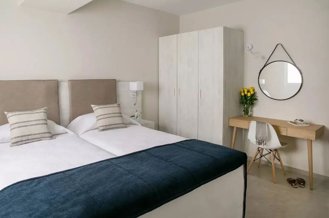 Hell eingerichtetes Schlafzimmer mit Betten, weißem Schrank und kleinem Schreibtisch.